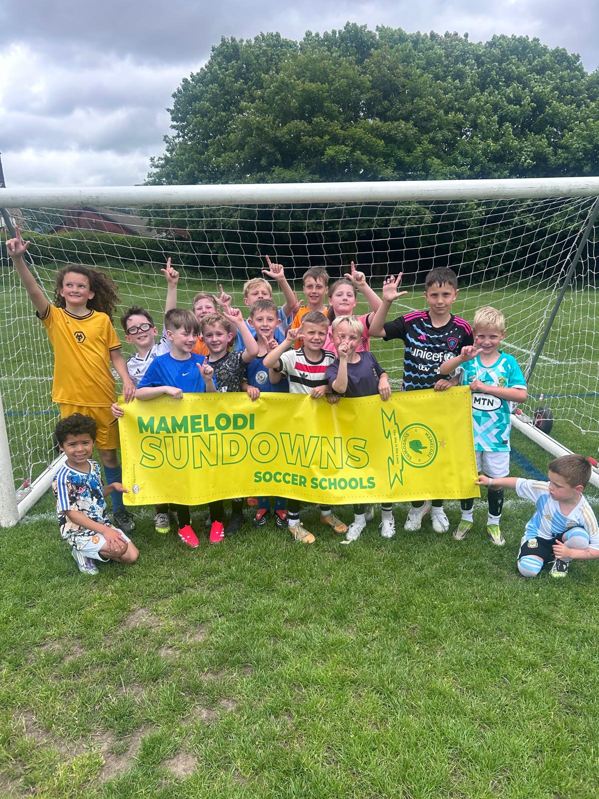 Players smiling together in front of a football goal with the Mamelodi Sundowns Soccer Schools banner
